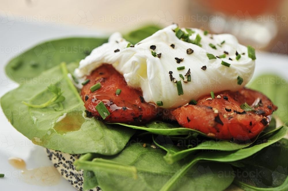 poached egg with roasted tomato, spinach leaves and a bagel - Australian Stock Image
