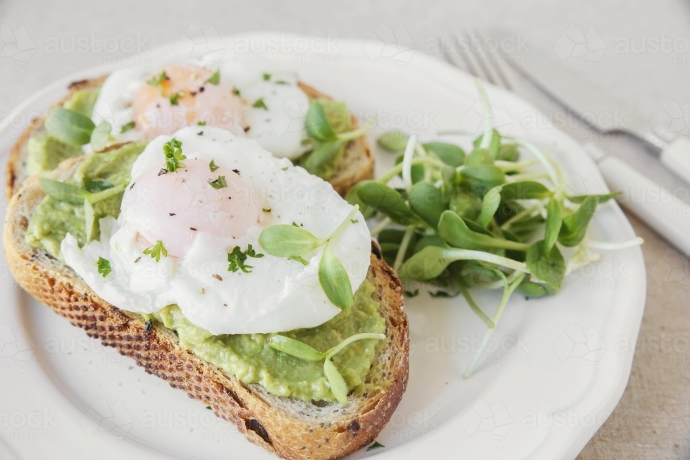 Poached eggs with avocado and sunflower sprout on sourdough toasts - Australian Stock Image