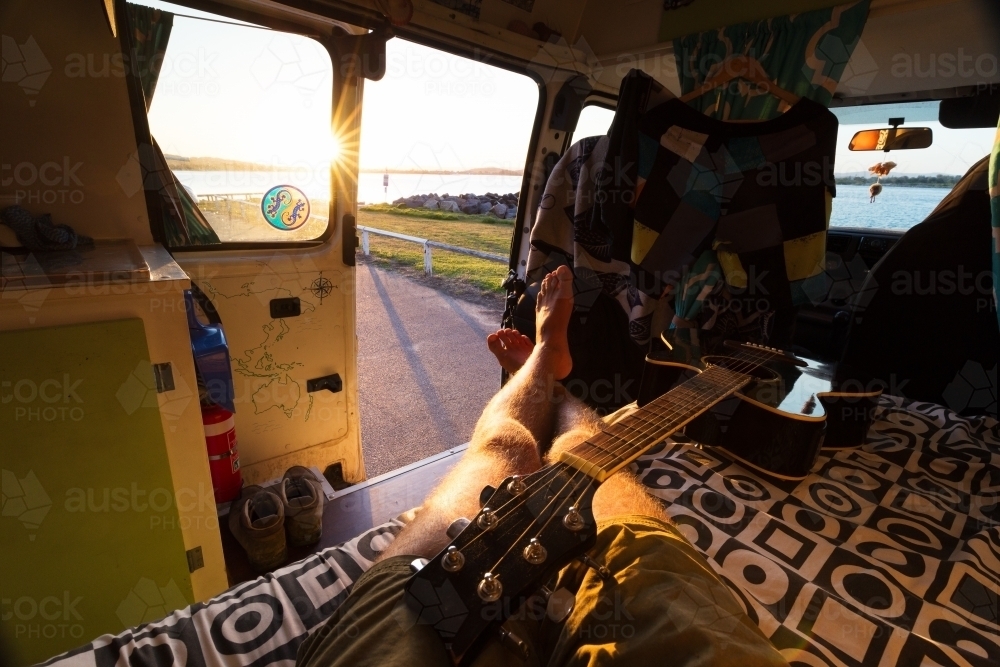 Point of view relaxed man in van life camper van with guitar and sunset - Australian Stock Image