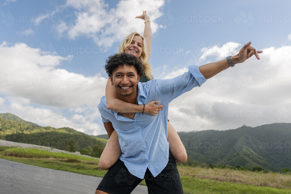 Polynesian man giving a Caucasian woman a piggyback ride on a country road - Australian Stock Image