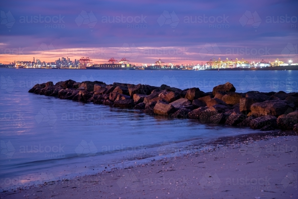 Port Botany at dusk with beach and rock groyne in foreground - Australian Stock Image