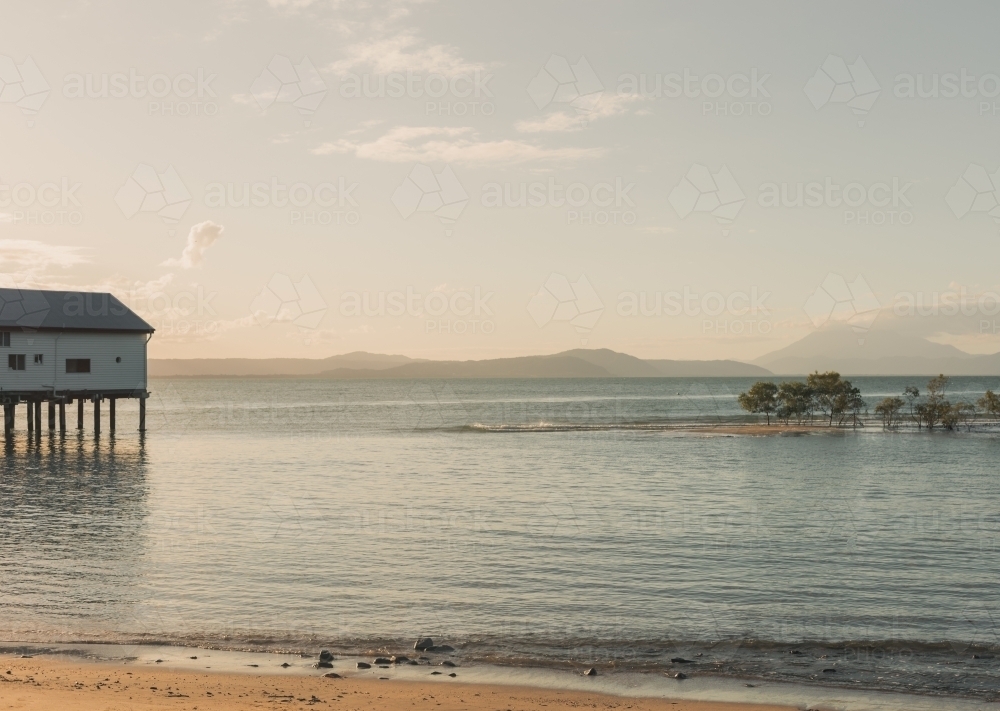 Port Douglas Sugar Wharf on stilts over the calm ocean in, with distant hills and beautiful dusk sky - Australian Stock Image
