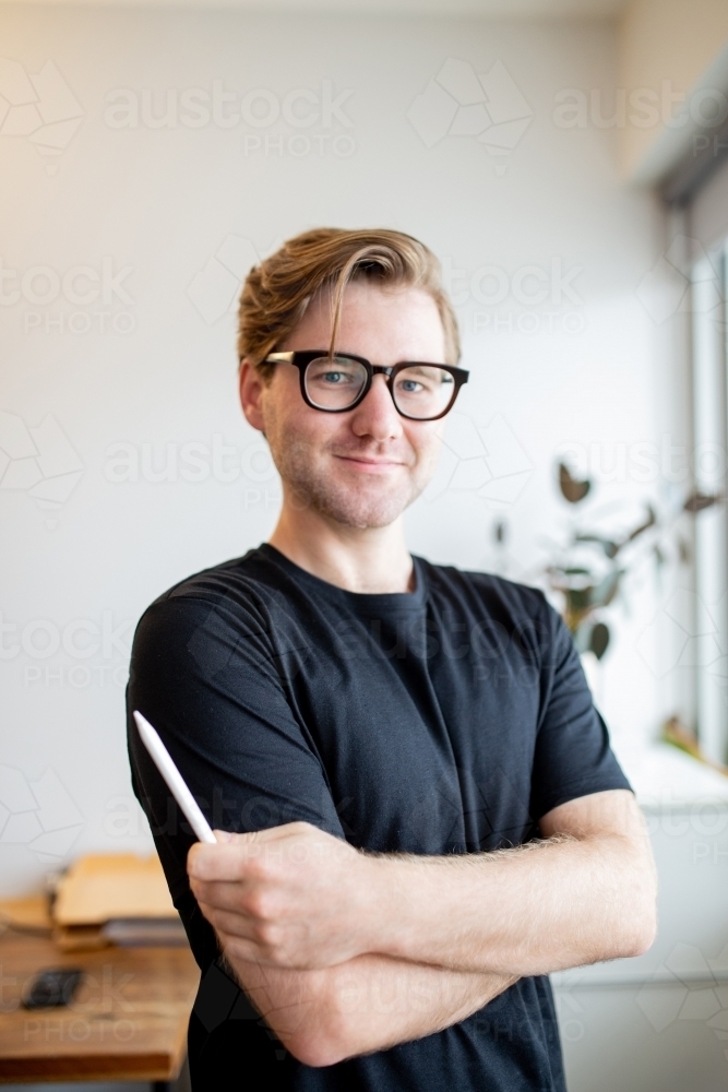 Man wearing glasses standing with a digital pencil in his hand in an office - Australian Stock Image