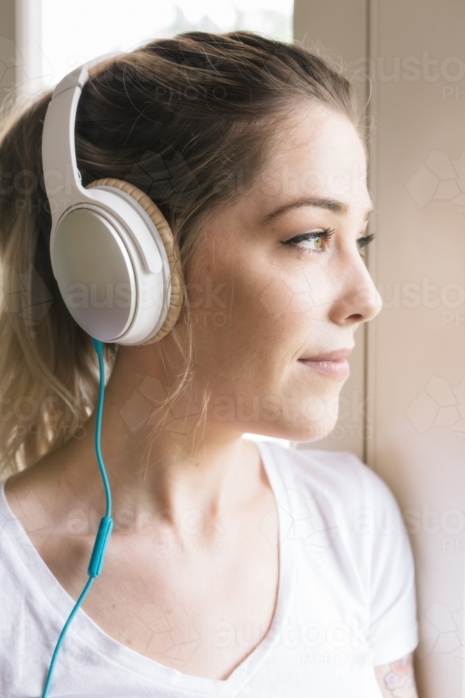 Portrait of a beautiful girl listening to music looking outside - Australian Stock Image