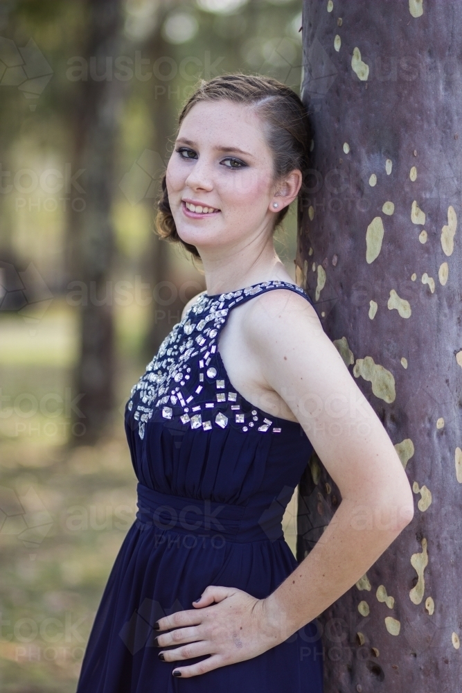 Portrait of a beautiful teen girl leaning against a gum tree dressed up for year 10 formal - Australian Stock Image