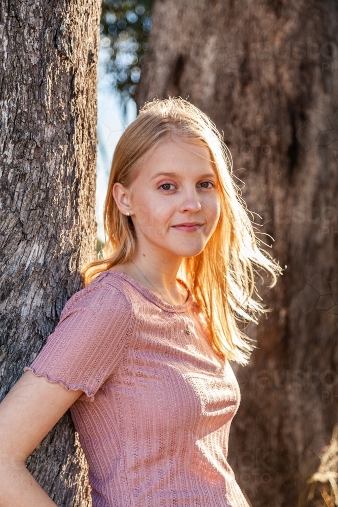 Portrait of a blond teen girl leaning against a tree - Australian Stock Image