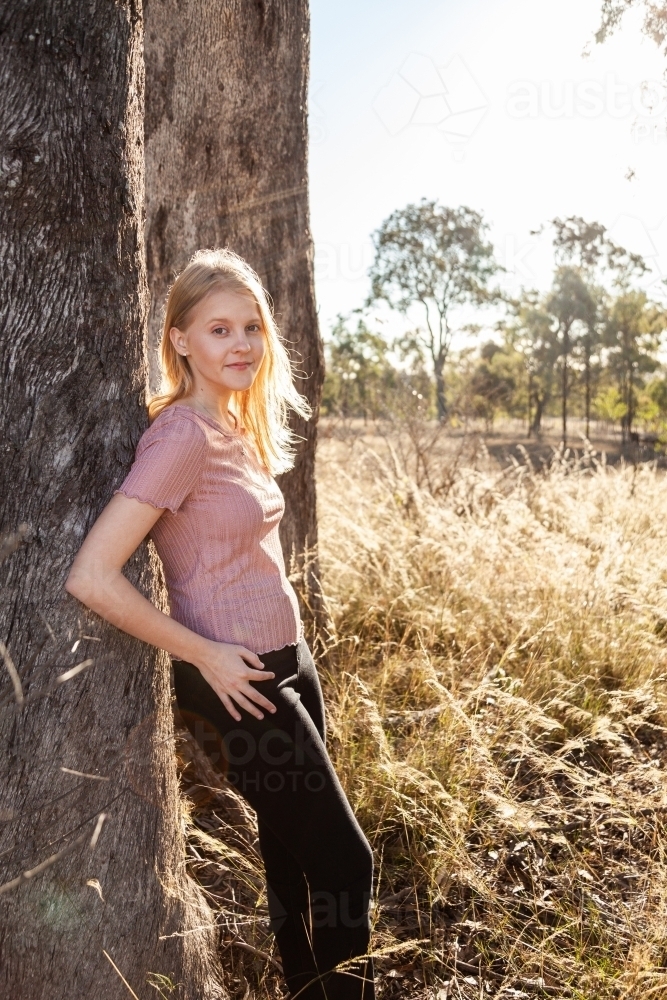 Portrait of a blond teen girl leaning against a tree - Australian Stock Image