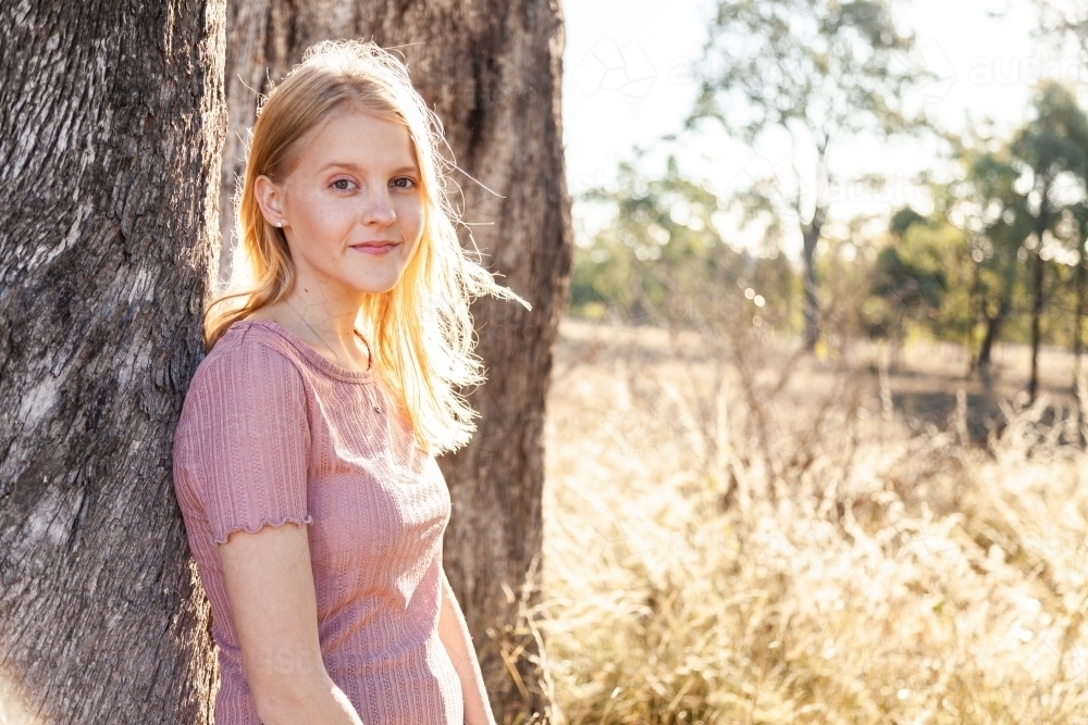 Portrait of a blond teen girl leaning against a tree - Australian Stock Image