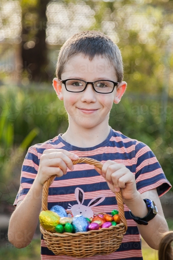 Portrait of a boy holding up basket full of Easter eggs - Australian Stock Image