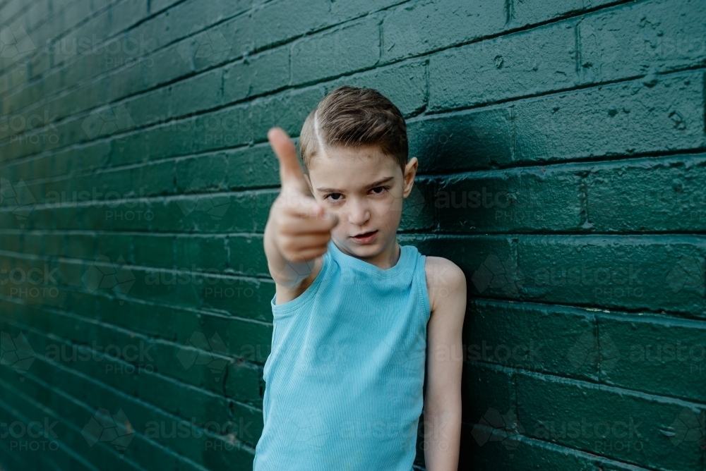 Portrait of a cool, young boy with serious attitude making a finger gun gesture - Australian Stock Image