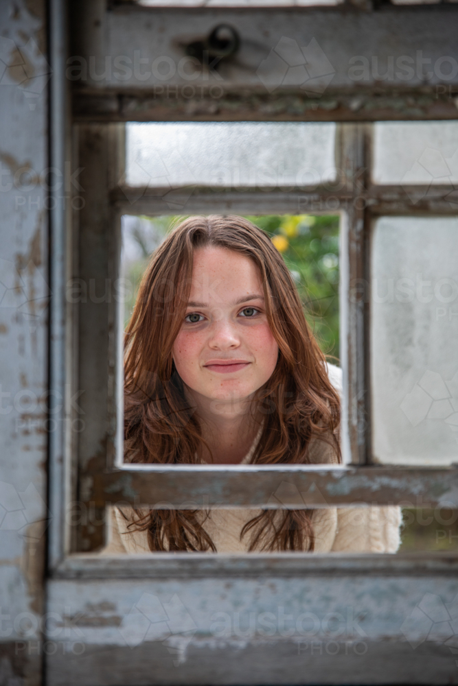 Portrait of a female looking through an old window - Australian Stock Image