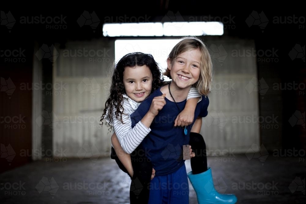 Portrait of a girl carrying her friend with background of dimly lit shed - Australian Stock Image