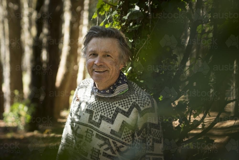 Portrait of a happy man leaning against a vine covered tree in forest - Australian Stock Image