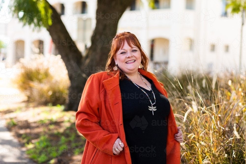 Portrait of a happy middle aged person wearing orange jacket in park - Australian Stock Image