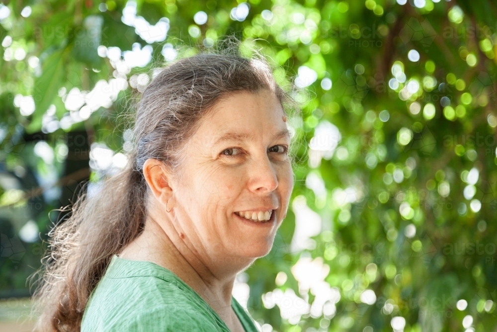 Portrait of a happy middle aged woman standing under green tree - Australian Stock Image