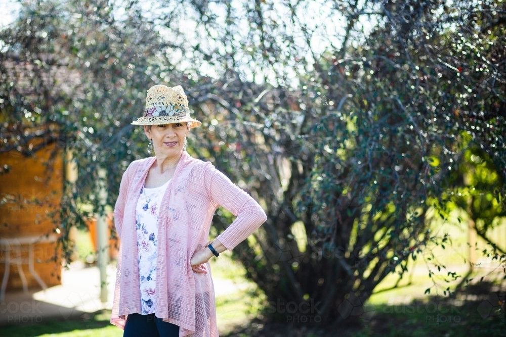 Portrait of a happy senior woman in a hat outside in winter garden - Australian Stock Image