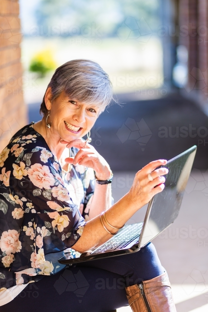Portrait of a happy smiling middle aged woman working on her laptop outside - Australian Stock Image
