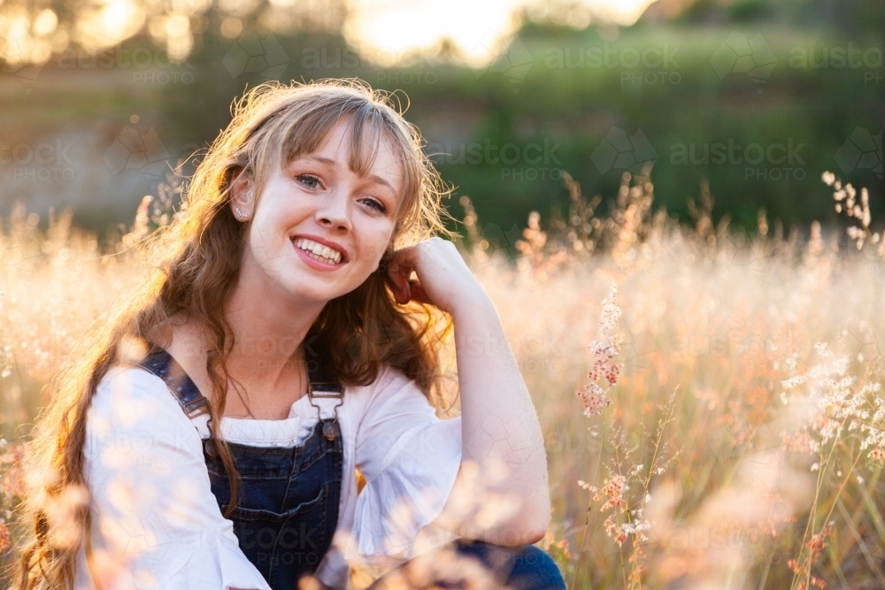 Portrait of a happy smiling young woman at sunset in fluffy grass - Australian Stock Image