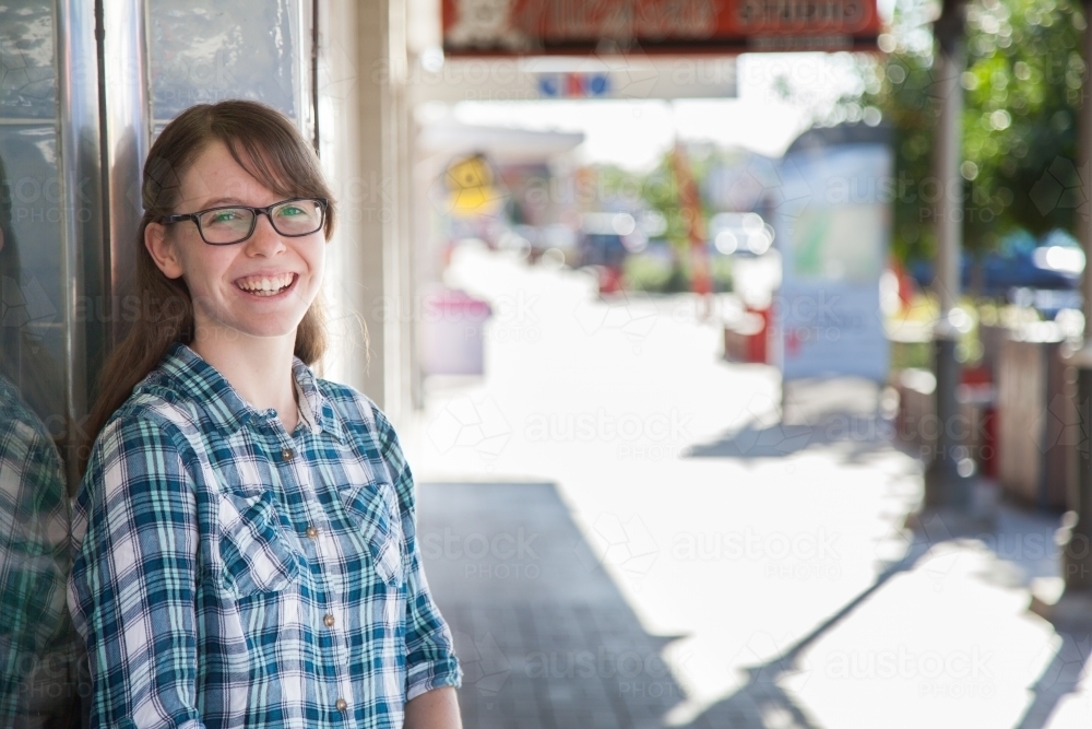 Portrait of a happy teen person leaning against shop window - Australian Stock Image