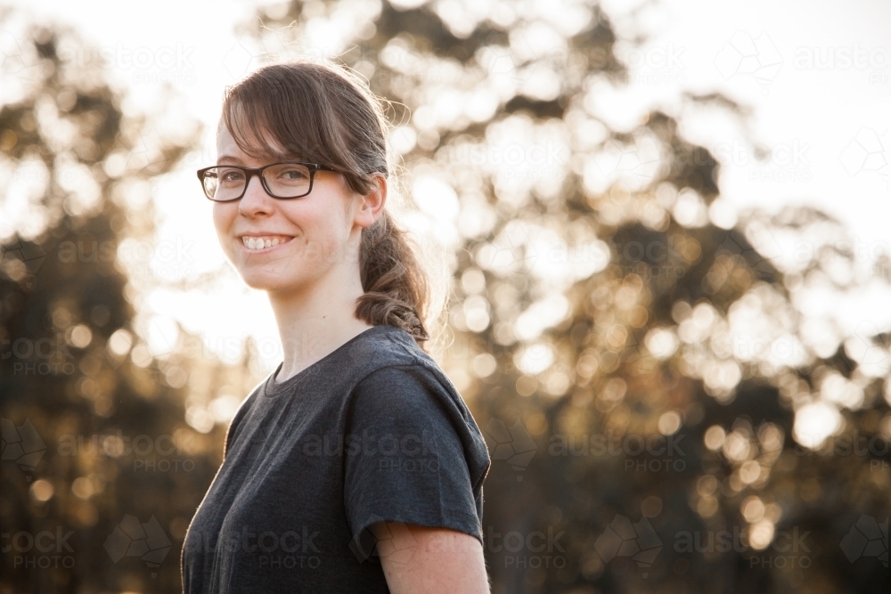 Portrait of a happy teenage girl with glasses smiling outside with brown bokeh copy space - Australian Stock Image