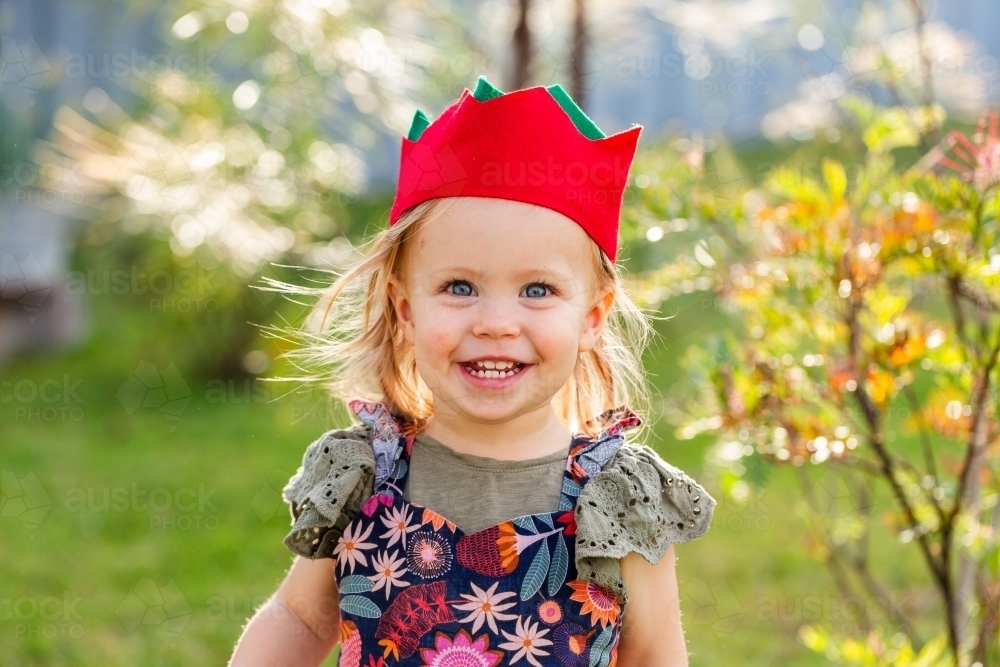 Portrait of a happy toddler girl outside in felt Christmas cracker hat - Australian Stock Image