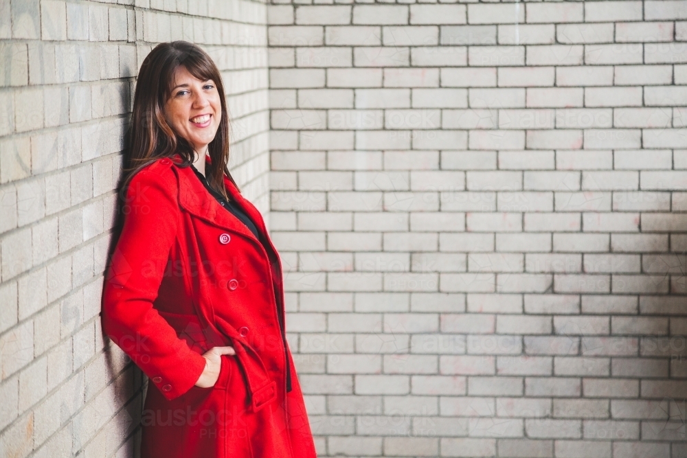 Image of Portrait of a happy woman in red jacket beside a brick wall ...