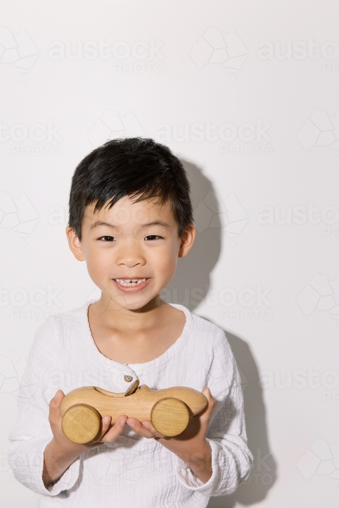 Portrait of a happy young boy holding a toy car on white background - Australian Stock Image