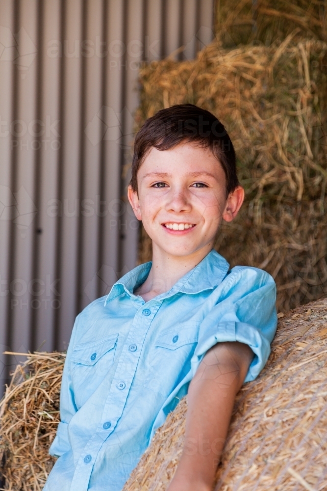 Portrait of a happy young boy on hay bales in a shed - Australian Stock Image
