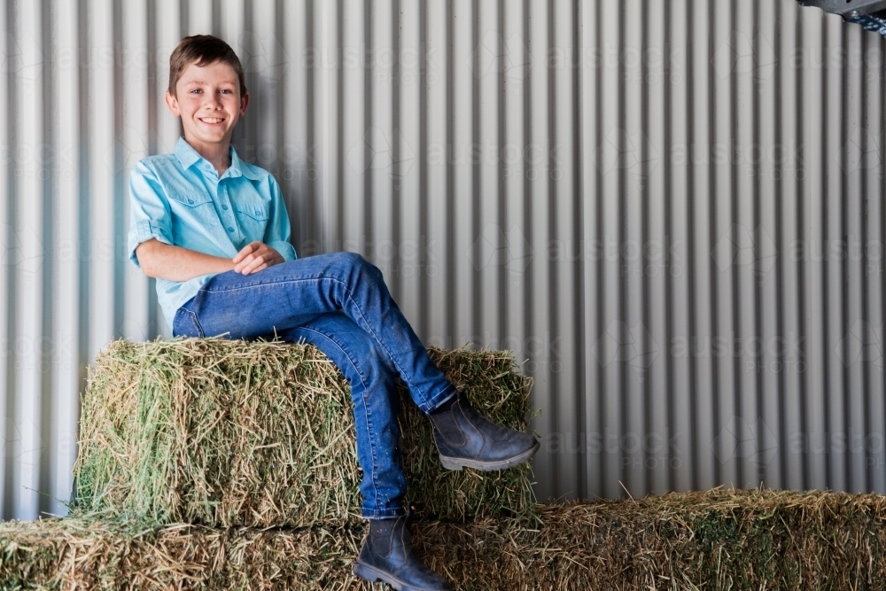 Portrait of a happy young boy on hay bales in a shed - Australian Stock Image