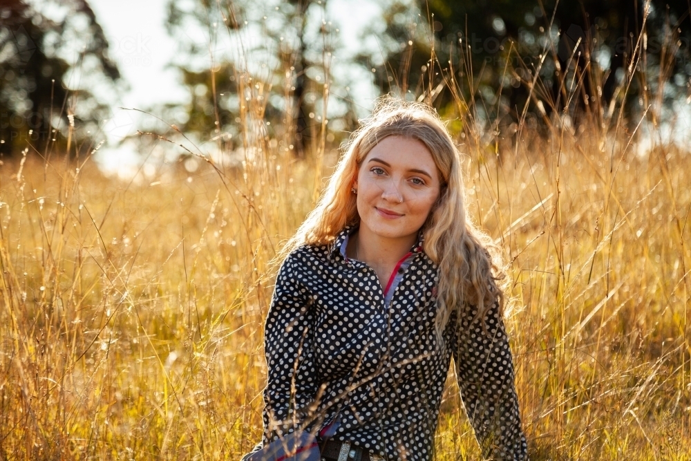 Portrait of a happy young country woman sitting in golden grass - Australian Stock Image