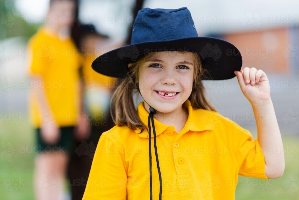 Portrait of a happy young school girl outside wearing a hat for sun protection - Australian Stock Image