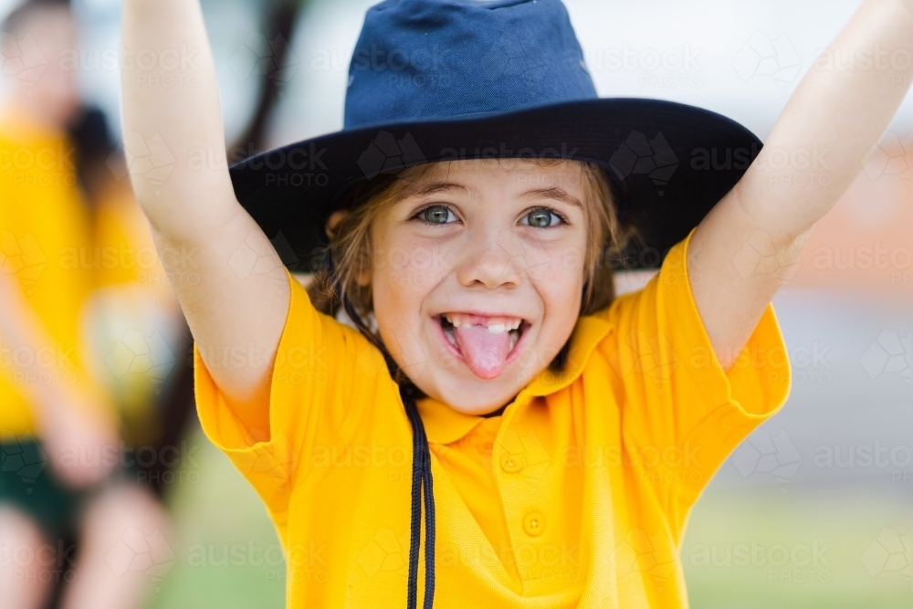 Portrait of a happy young school girl outside wearing a hat for sun protection - Australian Stock Image