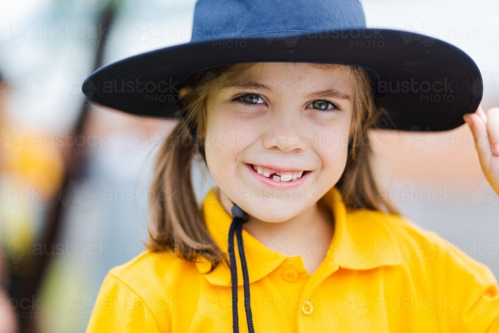 Portrait of a happy young school girl outside wearing a hat for sun protection - Australian Stock Image