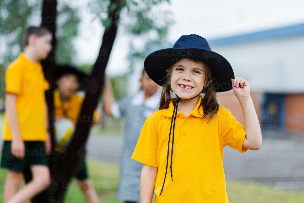 Portrait of a happy young school girl outside wearing a hat for sun protection - Australian Stock Image