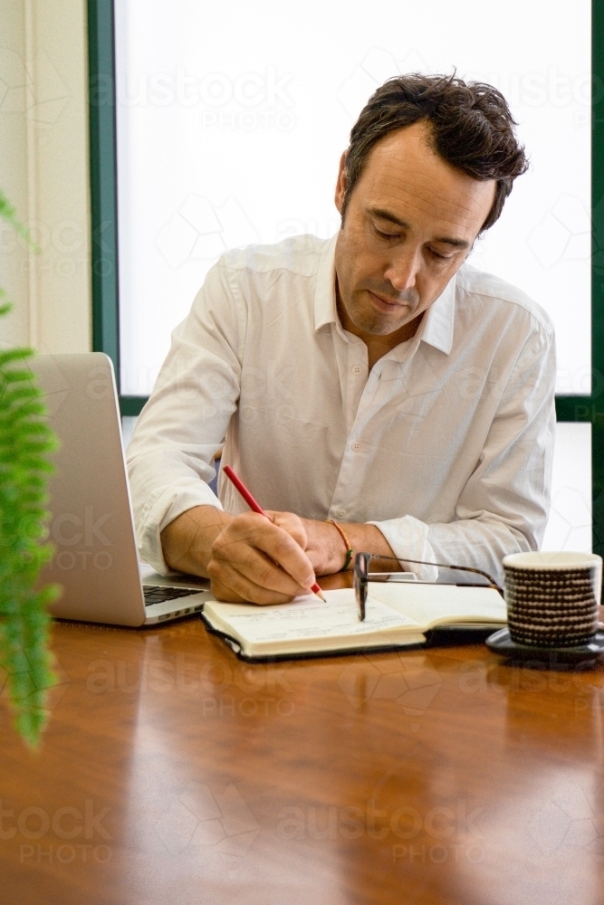 Portrait of a male office worker sitting with laptop and note book at a meeting table - Australian Stock Image