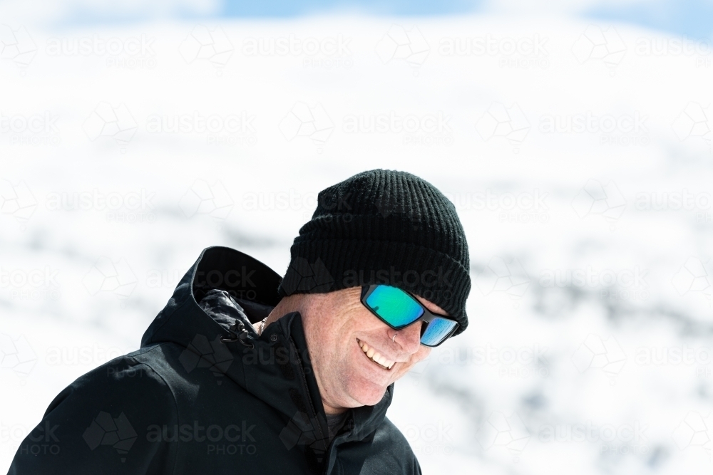 Portrait of a man looking down dressed in warm black outdoor coat and cap with blurred snow-covered - Australian Stock Image