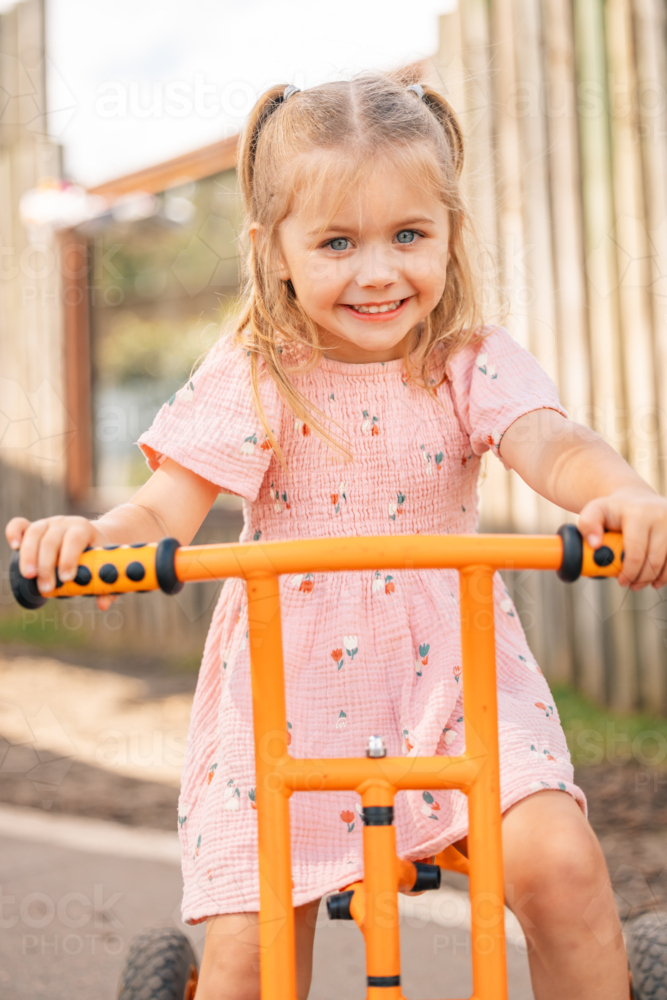 Portrait of a preschool age girl riding a orange trike at kindergarten - Australian Stock Image