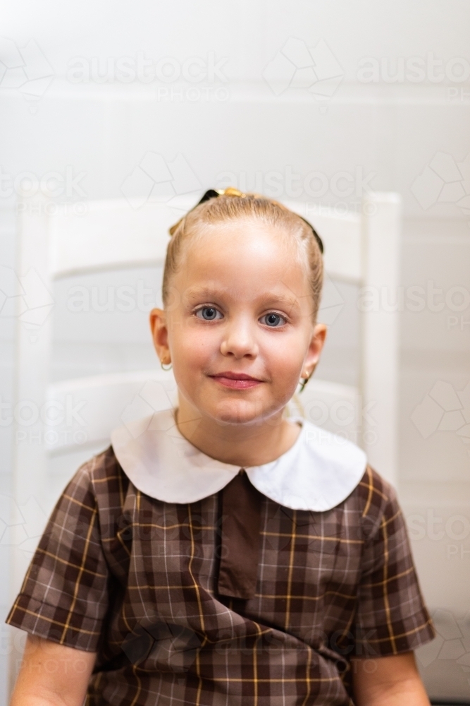 Portrait of a school girl in uniform sitting on chair at home before school - Australian Stock Image