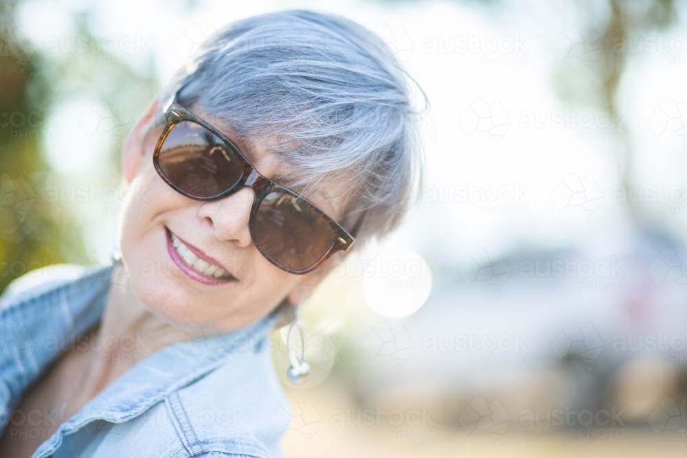 portrait of a senior woman in the garden wearing sunglasses - Australian Stock Image