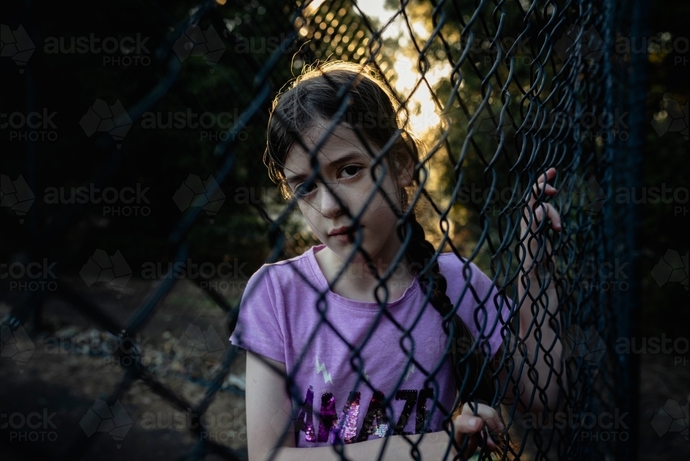 Portrait of a serious, young girl looking through a wire fence - Australian Stock Image