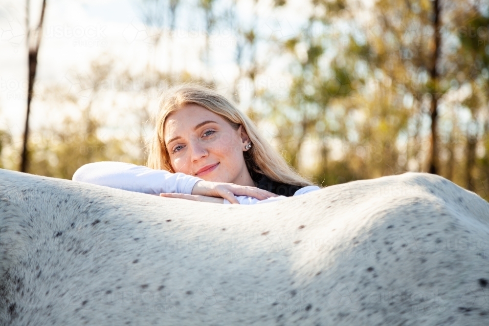 Portrait of a smiling blonde teen resting on her horse - Australian Stock Image