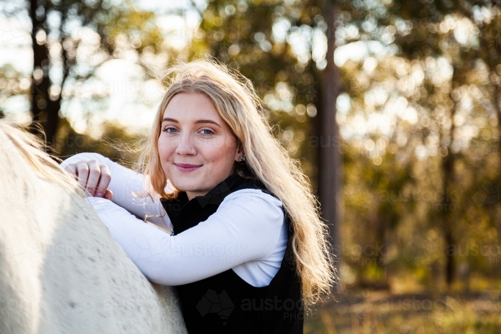 Portrait of a smiling blonde teen resting on her horse - Australian Stock Image