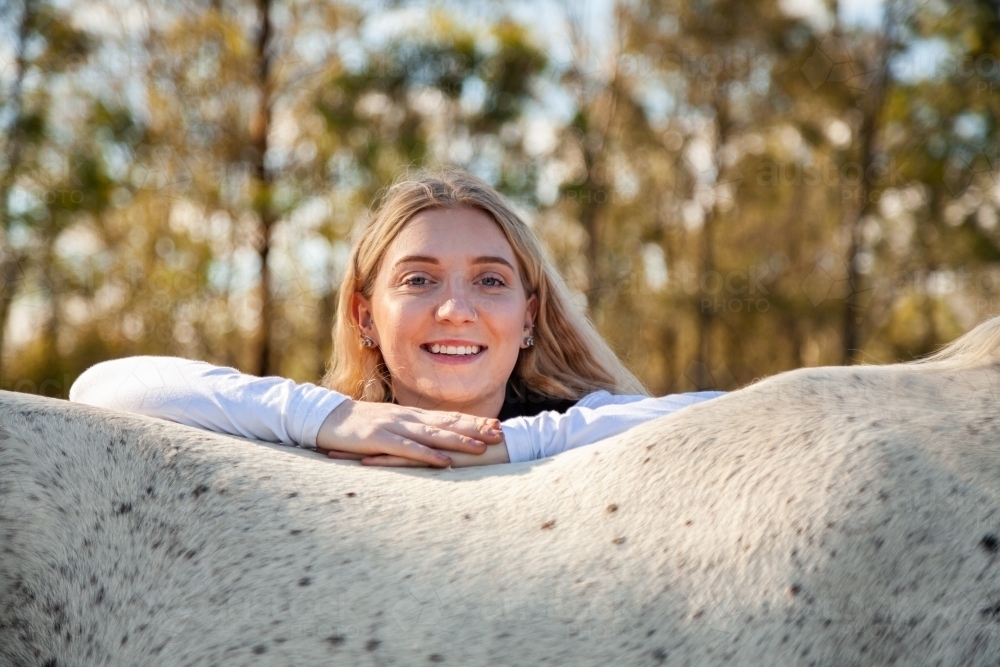 Portrait of a smiling blonde teen resting on her horse - Australian Stock Image