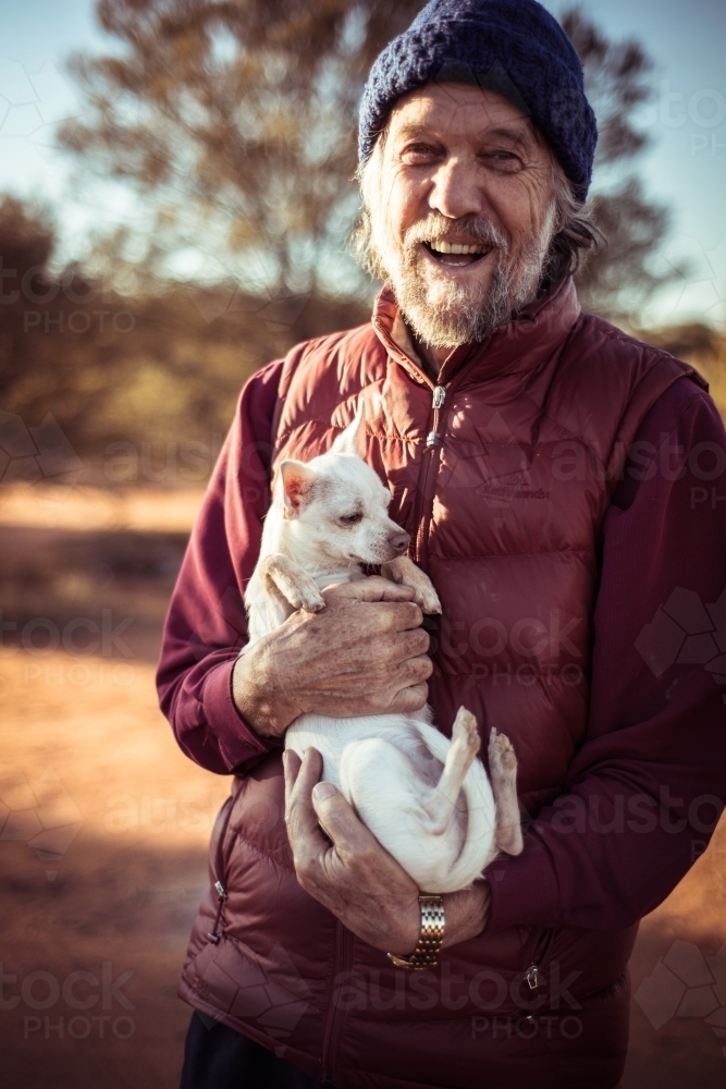 Portrait of a smiling older man holding a small dog  in the desert - Australian Stock Image