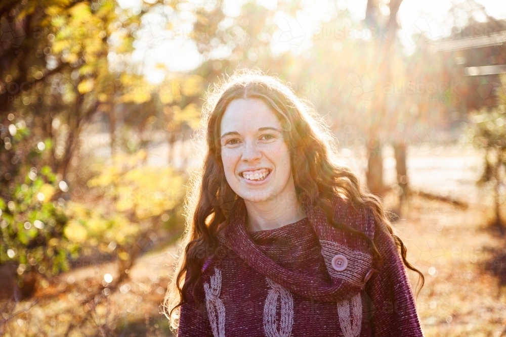 Portrait of a smiling young woman backlit by warm winter light - Australian Stock Image