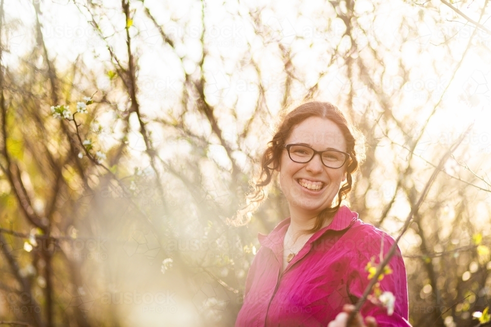 Portrait of a smiling young woman surrounded by white spring blossoms - Australian Stock Image