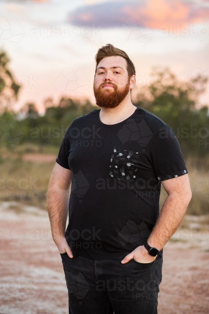 Portrait of a young aussie man with beard, outside at dusk wearing black t-shirt - Australian Stock Image