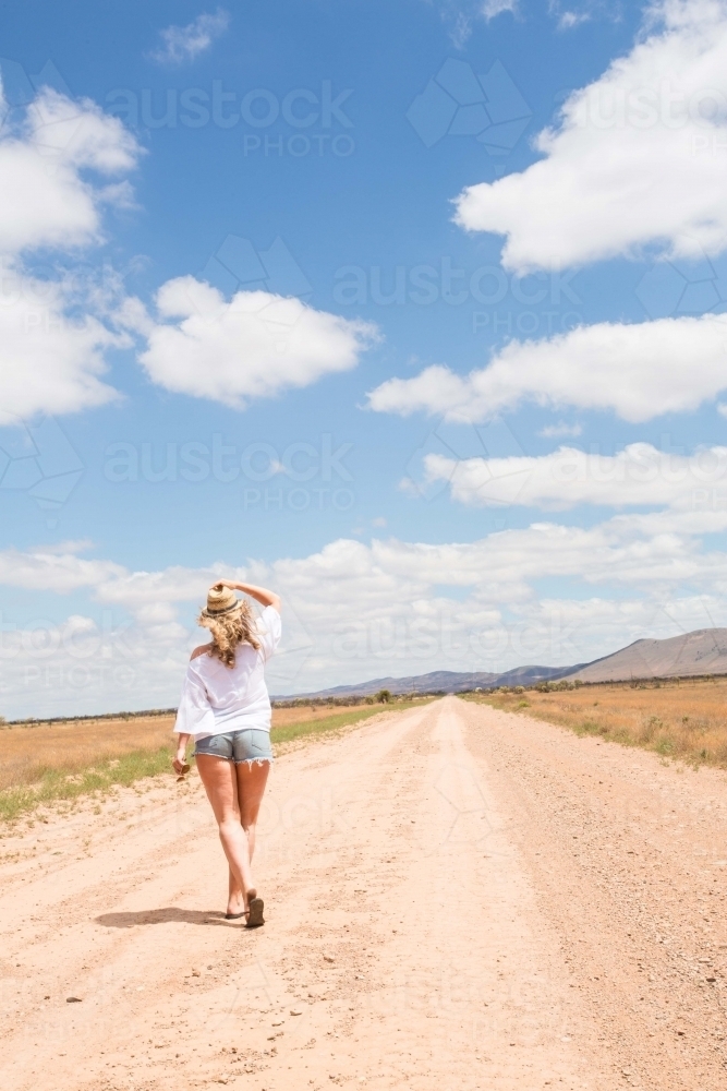 Portrait of a young blonde woman walking alone under blue skies and white clouds in the country side - Australian Stock Image