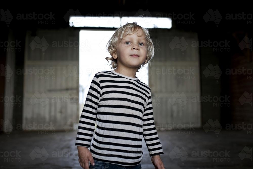 Portrait of a young boy with with background of dimly lit shed - Australian Stock Image