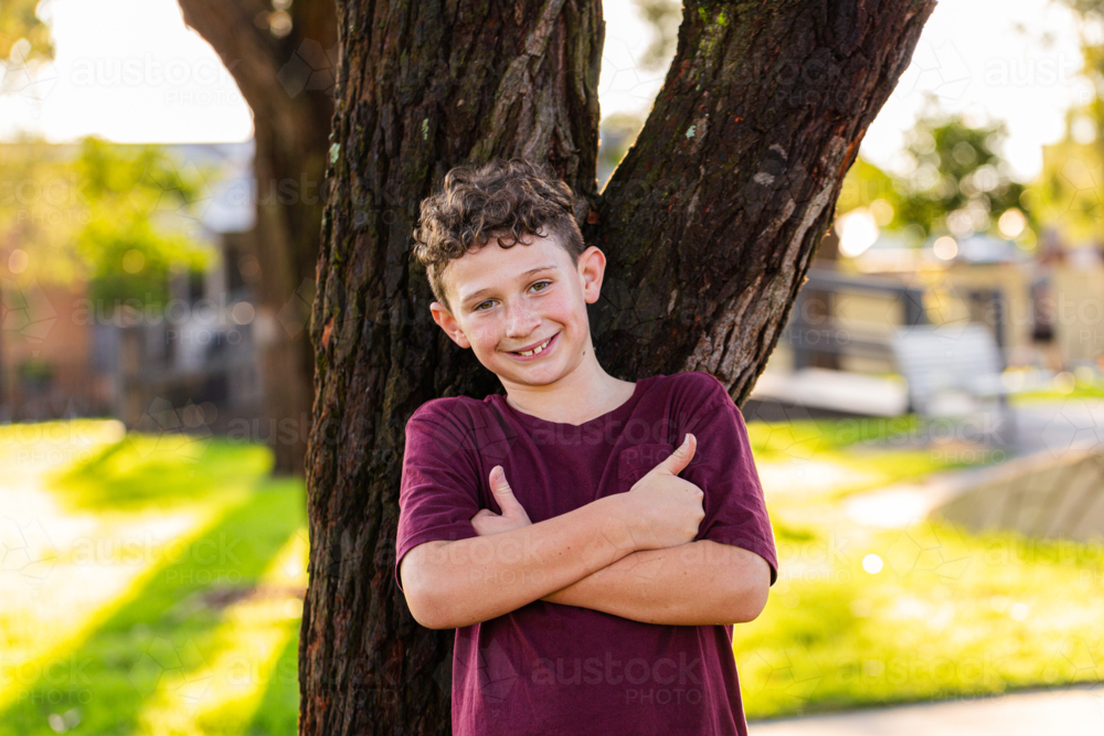 portrait of a young confident aussie 9yo boy leaning against tree - Australian Stock Image